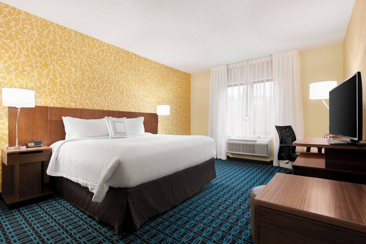 A hotel room with a large bed, two bedside tables with lamps, a desk with a television, and a patterned carpet.