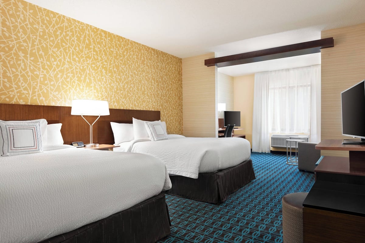 A hotel room with two beds, a desk, a TV, and a window with curtains.