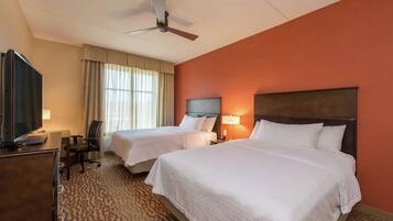 A hotel room with two beds, a desk, a television, and a ceiling fan.