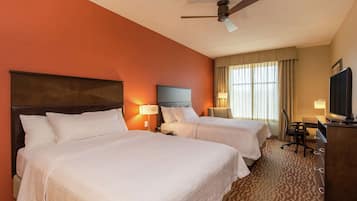 Una habitación de hotel con dos camas, un escritorio, una silla, un televisor y un ventilador de techo.