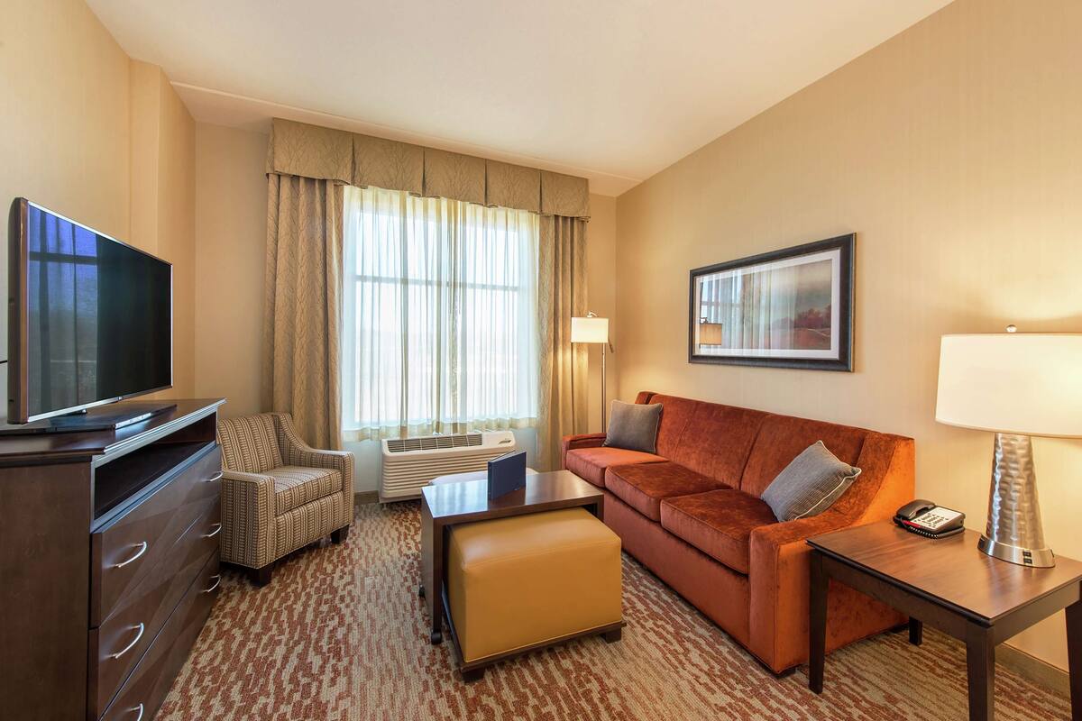 Een hotelkamer met een televisie, een bank, een stoel, een tafel, een lamp en een schilderij aan de muur.