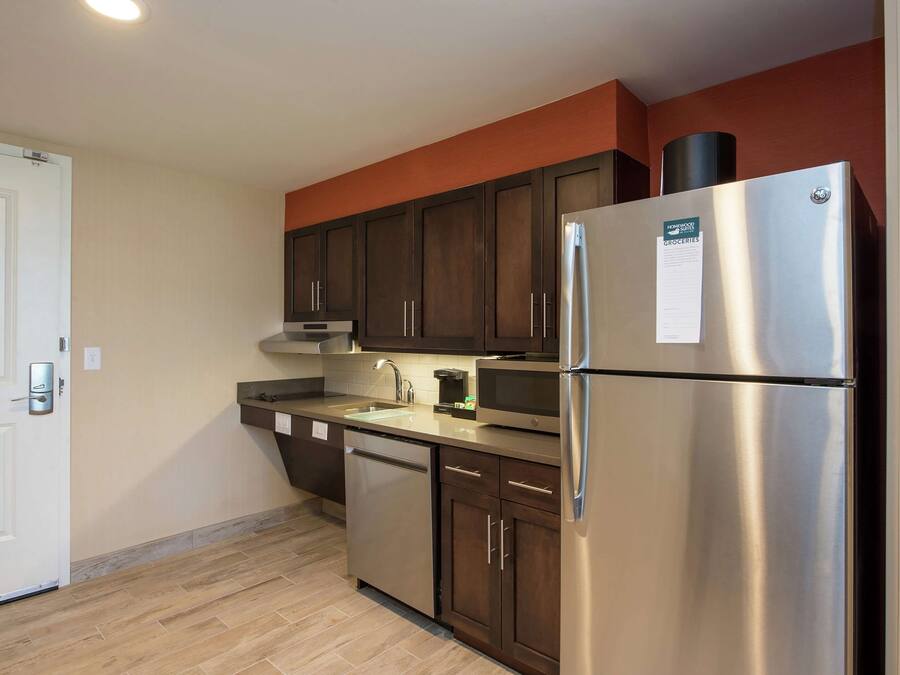 A modern kitchen with stainless steel appliances, dark wooden cabinets, and a beige tiled backsplash.