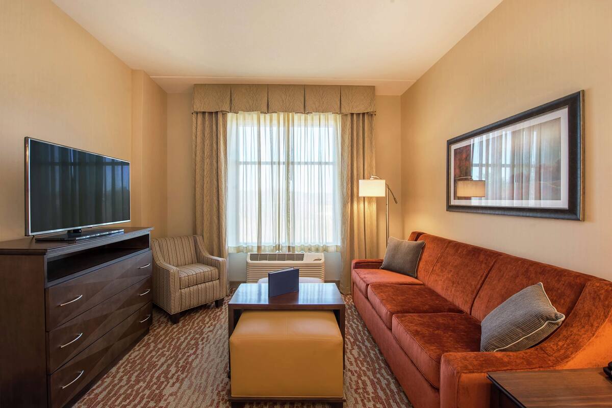 Een hotelkamer met een flatscreen televisie, een bank, een stoel, een salontafel en een ingelijst kunstwerk aan de muur.