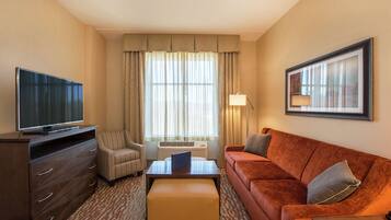 A hotel room with a flat-screen TV, a sofa, a chair, a coffee table, and a framed picture on the wall.