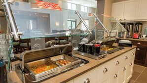 Zona de bufé con diversas opciones de comida, incluyendo hamburguesas y ensalada.