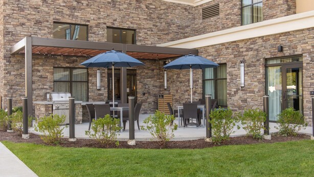 Un patio con mobiliario exterior y una parrilla, rodeado de muros de piedra y pequeñas plantas.