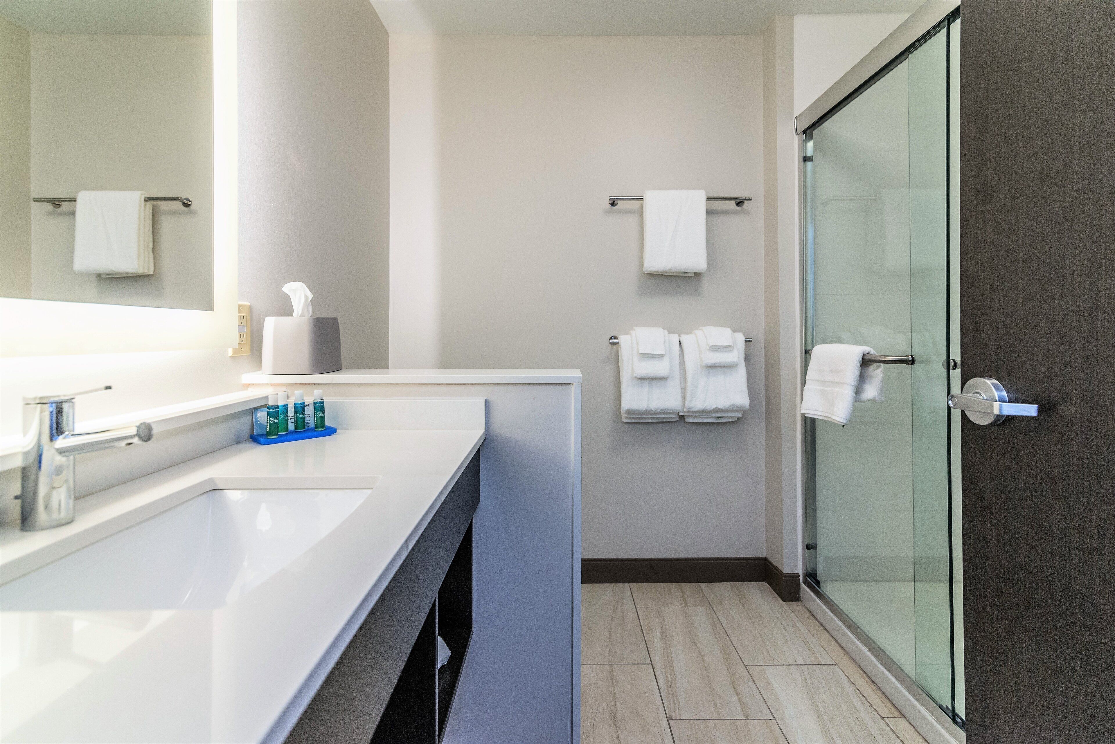 Un bany modern amb un lavabo blanc, un box de dutxa de vidre i tovalloles ordenades.