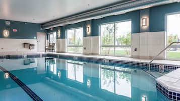 A swimming pool with clear water, surrounded by walls with windows, and an exit sign.