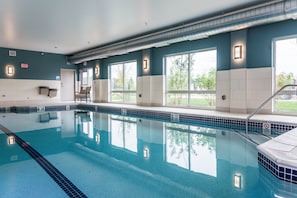 A swimming pool with clear water, surrounded by walls with windows, and an exit sign. - Holiday Inn Express & Suites Allen Park by IHG (Allen Park)