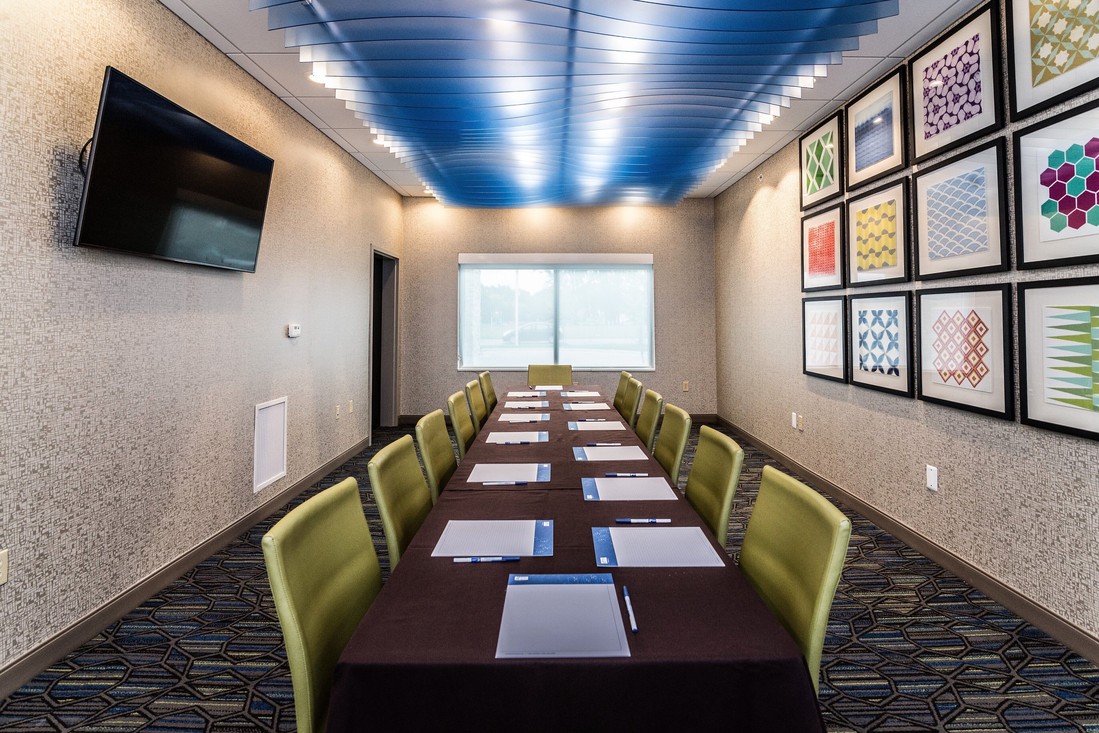 A conference room with a long table, chairs, a flat-screen TV, and framed artwork on the walls.
