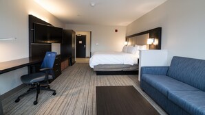 A modern hotel room with a bed, a desk with a chair, a sofa, a flat-screen TV, and a bedside lamp. - Holiday Inn Express & Suites Allen Park by IHG (Allen Park)