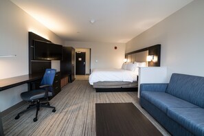A modern hotel room with a bed, a desk with a chair, a sofa, a flat-screen TV, and a bedside lamp. - Holiday Inn Express & Suites Allen Park by IHG (Allen Park)