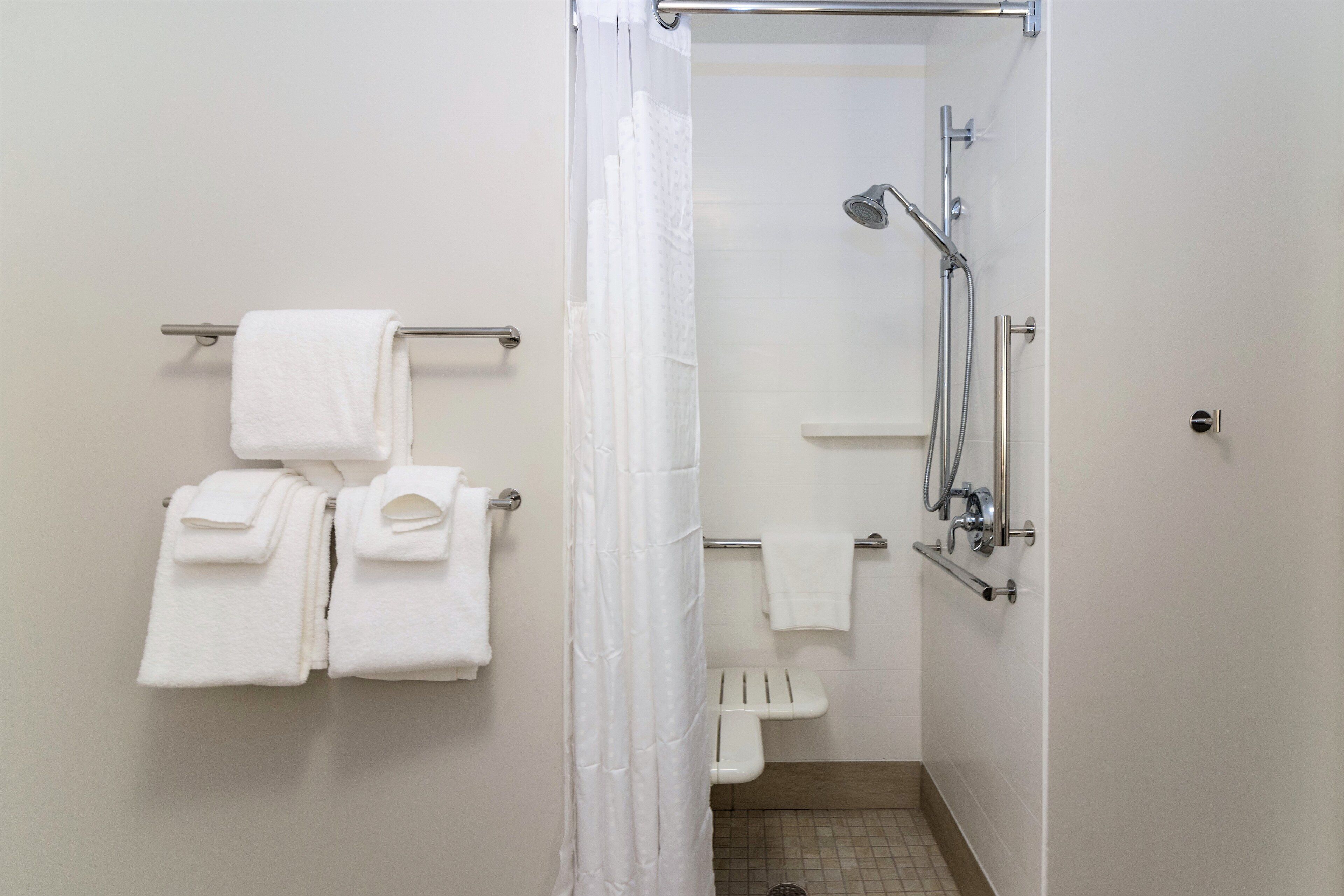 Een badkamer met een douche, een handdoekrek met opgevouwen handdoeken en een douchegordijn.