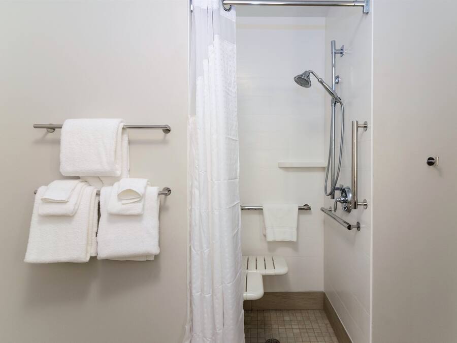 Een badkamer met een douche, een handdoekrek met opgevouwen handdoeken en een douchegordijn.
