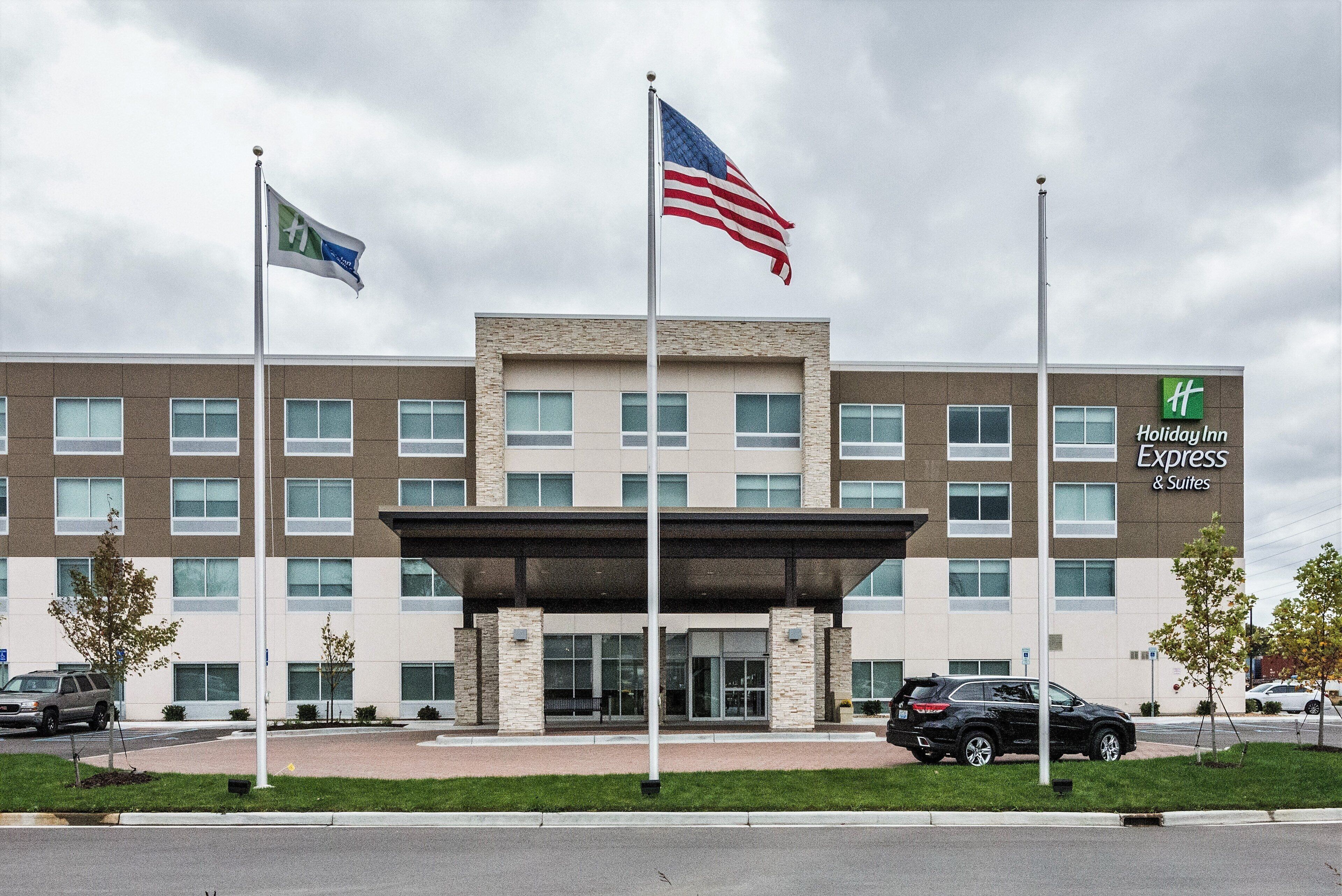 A Holiday Inn Express & Suites hotel with a modern architectural design, featuring a prominent entrance and multiple flags.