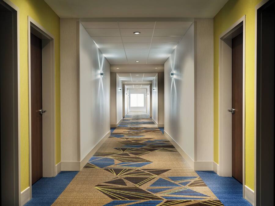 A hotel corridor with a patterned carpet, doors on both sides, and a ceiling with recessed lighting.