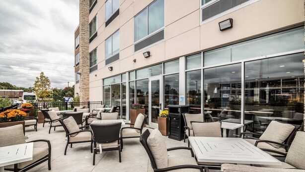 An outdoor patio area with wicker furniture and large windows overlooking a parking lot. - Holiday Inn Express & Suites Allen Park by IHG (Allen Park)