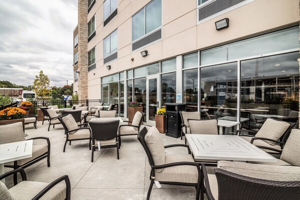 An outdoor patio area with wicker furniture and large windows overlooking a parking lot. - Holiday Inn Express & Suites Allen Park by IHG (Allen Park)
