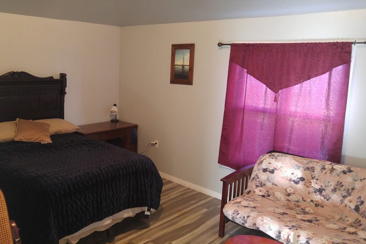 A bedroom with a bed, a nightstand, a lamp, a chair, and a window with curtains.
