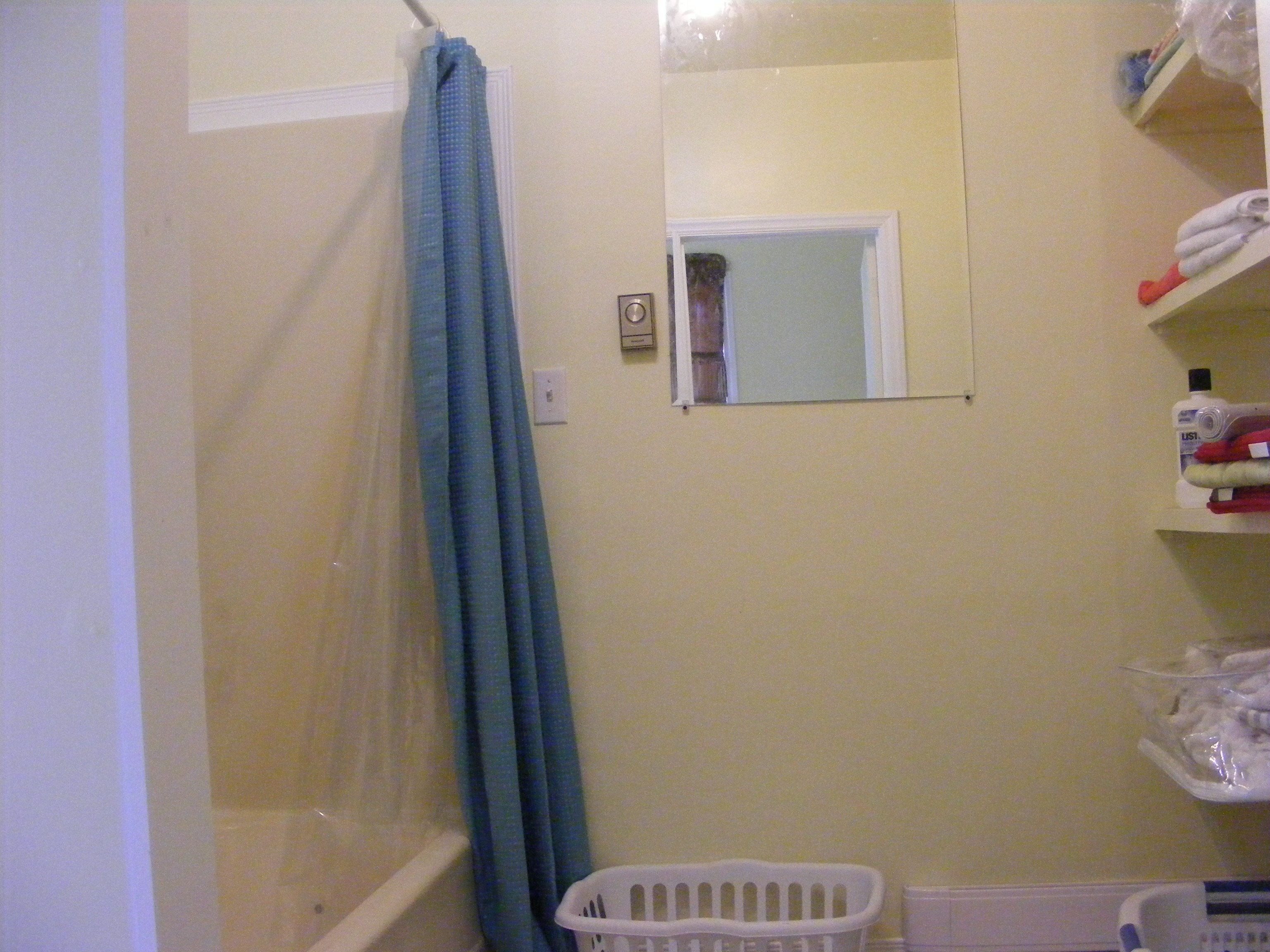 Un baño con ducha, un espejo, una cesta de plástico blanca y estantes con artículos de aseo.