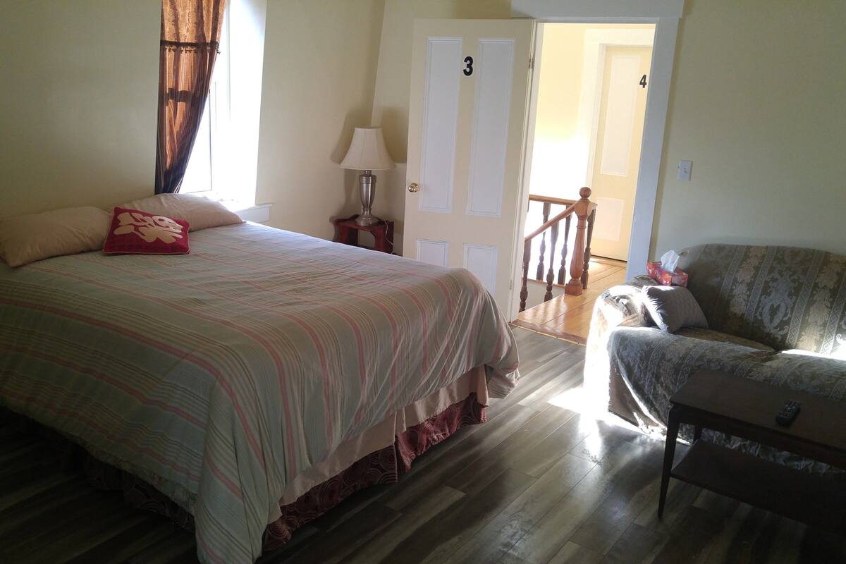 A bedroom with a bed, a chair, a nightstand, and a lamp.
