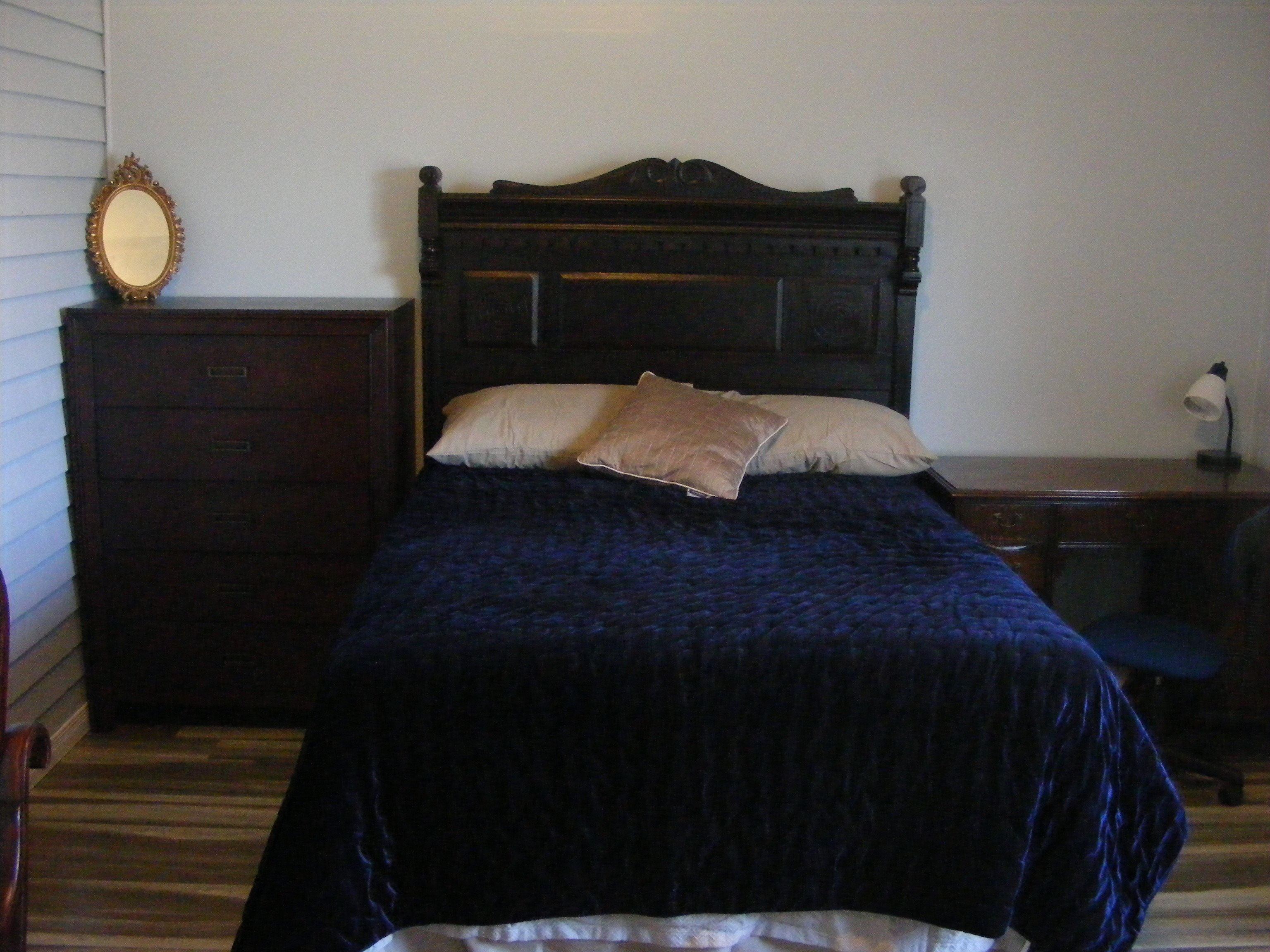 Un dormitorio con una cama de madera oscura, dos almohadas, un aparador y un escritorio con una lámpara.
