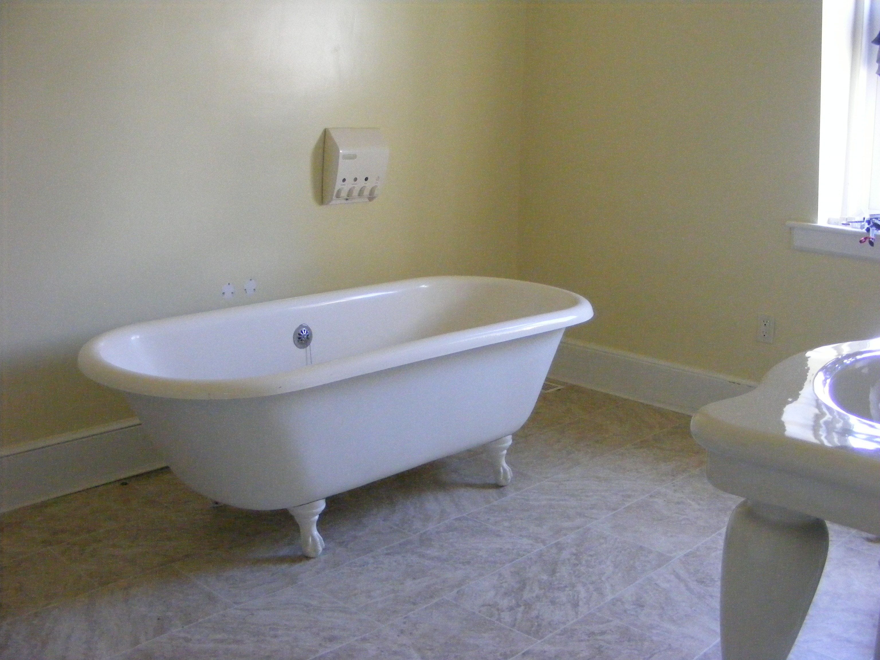 A bathroom with a clawfoot bathtub, a toilet, and a wall-mounted electrical outlet.