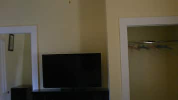 Un dormitorio con cama, ventilador de techo, cómoda, televisor y armario con ropa colgada.