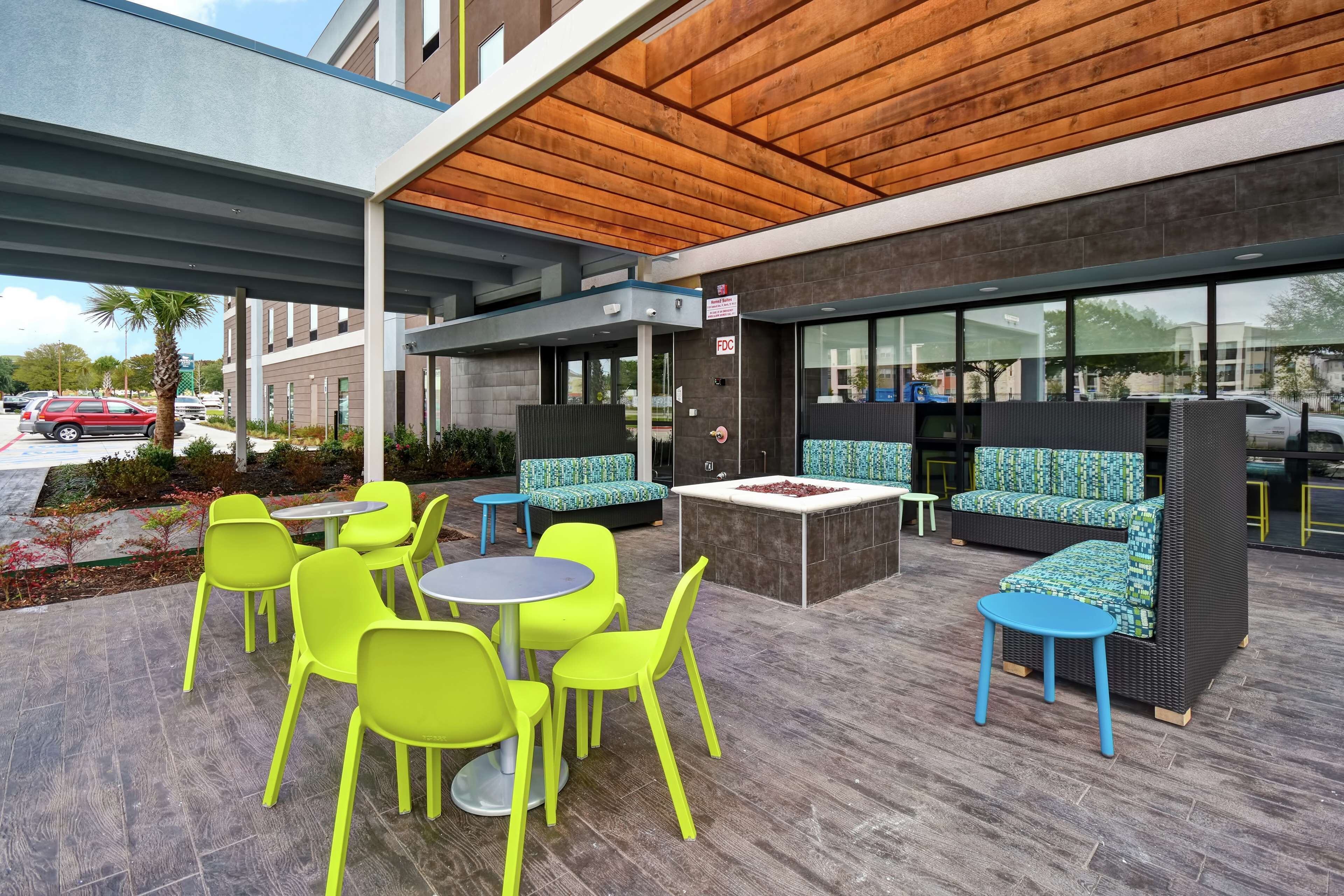 An outdoor seating area with bright green chairs and tables, a covered patio, and a modern building facade.