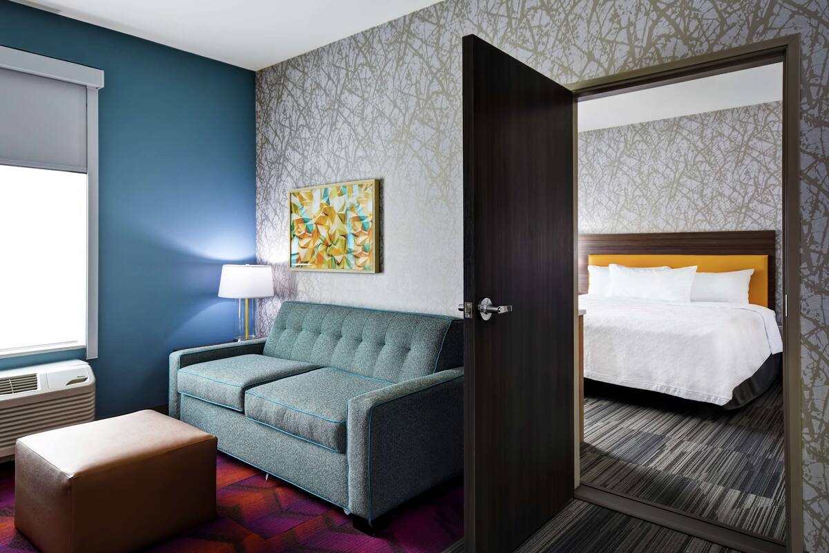 Een hotelkamer met een bank, nachtkastje met lamp, bed en groot raam.