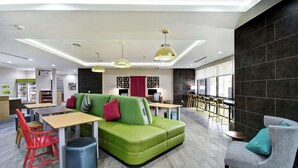 A modern lounge area with a green sofa, red and green chairs, a small table, and a grey armchair. - Home2 Suites by Hilton Fort Worth Fossil Creek (Fort Worth)