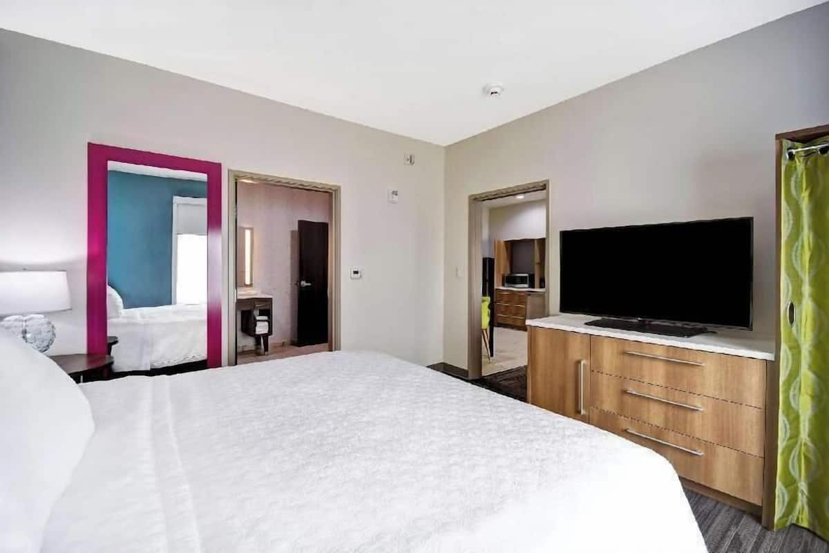 A hotel room with a bed, a television, a desk, and a bathroom visible through an open door.