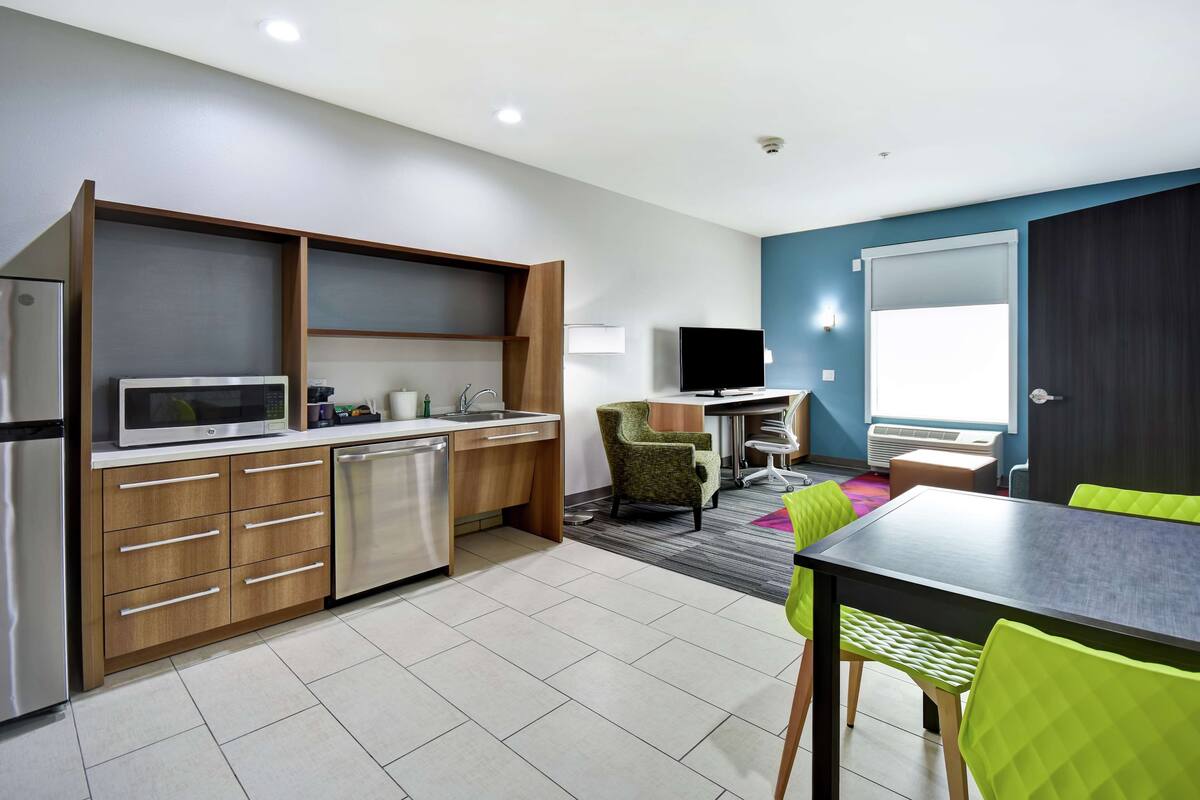 Een kleine keuken met moderne apparaten, een eethoek met een tafel en stoelen, en een televisie op de achtergrond.