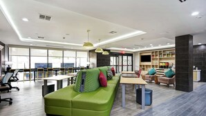A modern hotel lobby with a green sofa, seating area, and a large window providing a view. - Home2 Suites by Hilton Fort Worth Fossil Creek (Fort Worth)
