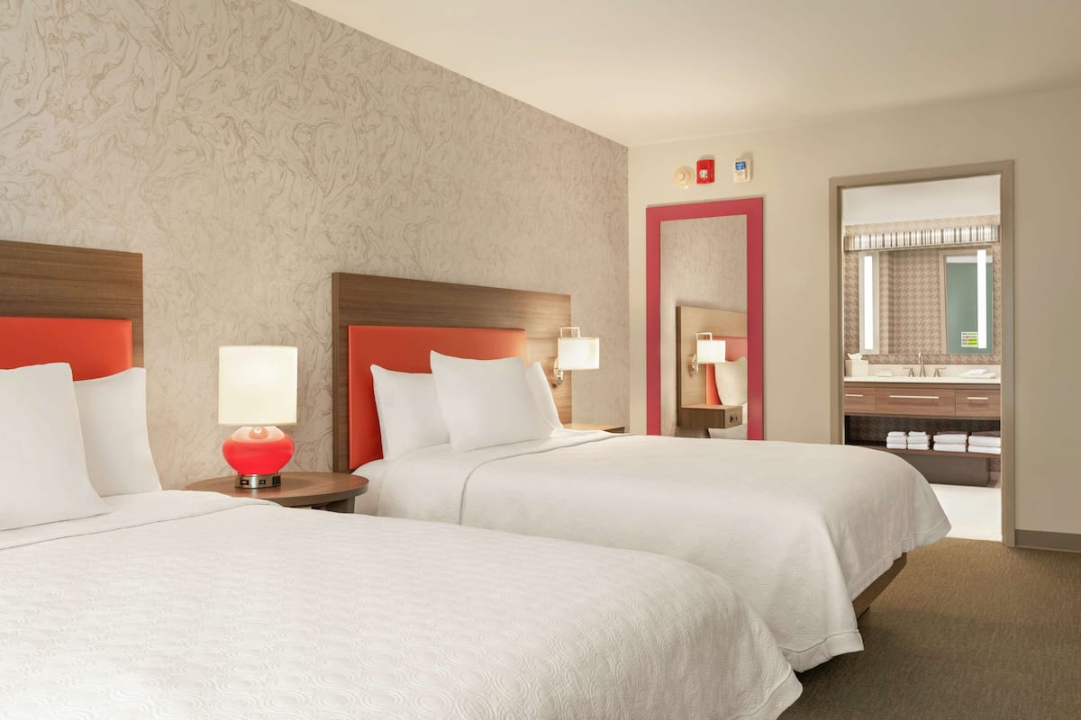 Een hotelkamer met twee bedden, een rode lamp, een spiegel en een zichtbare badkamer door een open deur.
