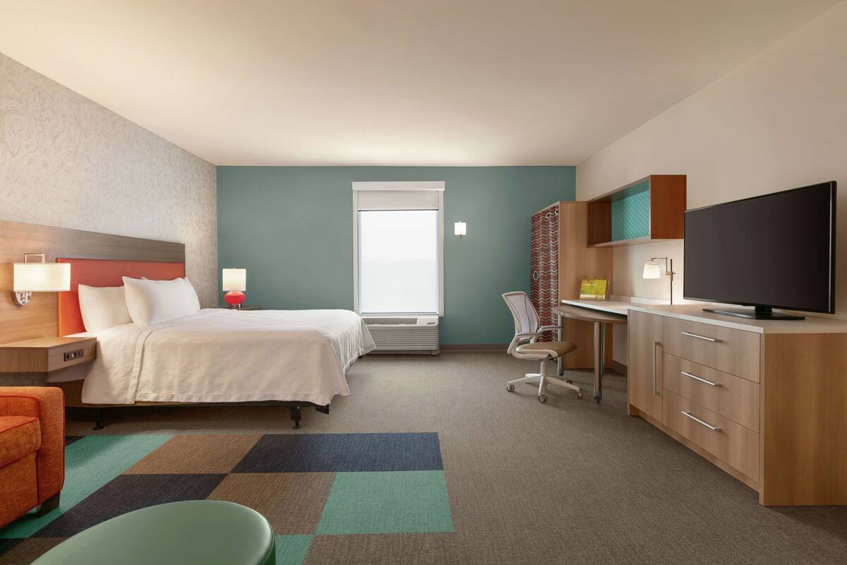 Een hotelkamer met een bed, bureau, stoel, televisie en een raam.