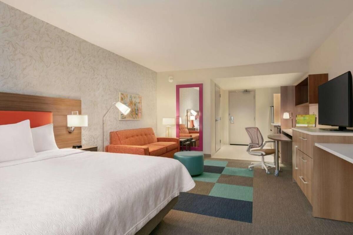 Een hotelkamer met een bed, een bureau, een stoel, een televisie en een badkamer zichtbaar door een geopende deur.