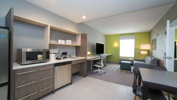 A modern kitchen with a microwave, sink, and dishwasher, a dining area with a table and chairs, and a TV in the background.