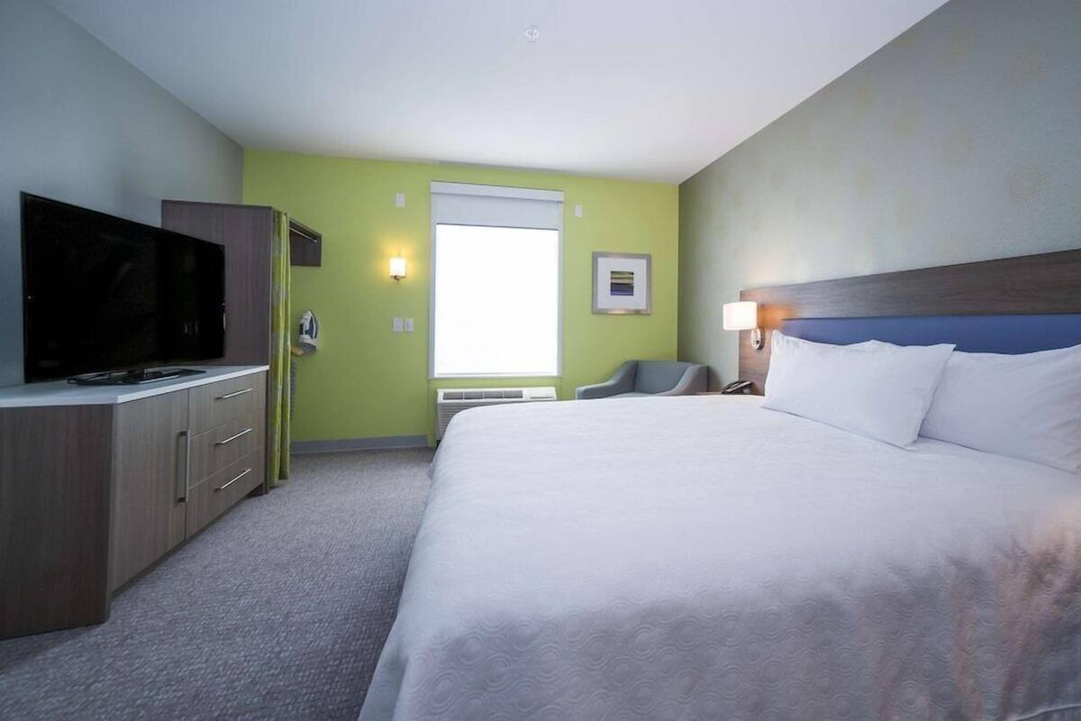 Hotellihuone, jossa on sänky, kaapissa oleva televisio, tuoli ja ikkuna.