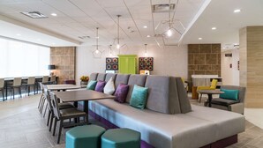 A modern hotel lobby with a large seating area, a reception desk, and a dining area. - Home2 Suites by Hilton Jackson Flowood Airport Area (Flowood)