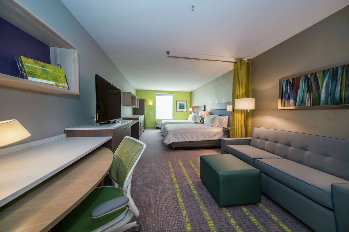Hotellihuone, jossa on työpöytä, tuoli, sänky, sohva ja televisio.