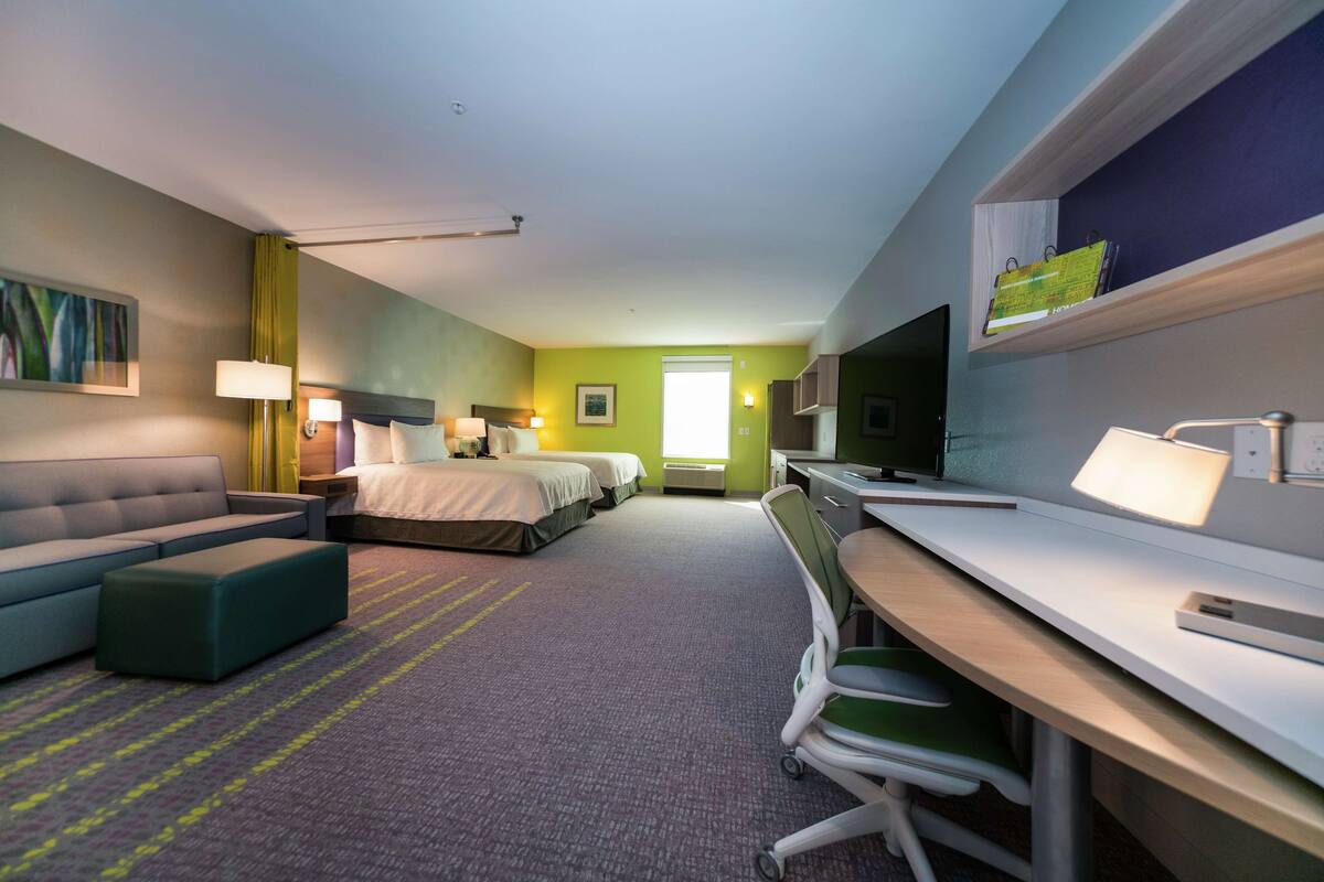 Hotellihuone, jossa on sänky, työpöytä, tuoli, sohva ja televisio.
