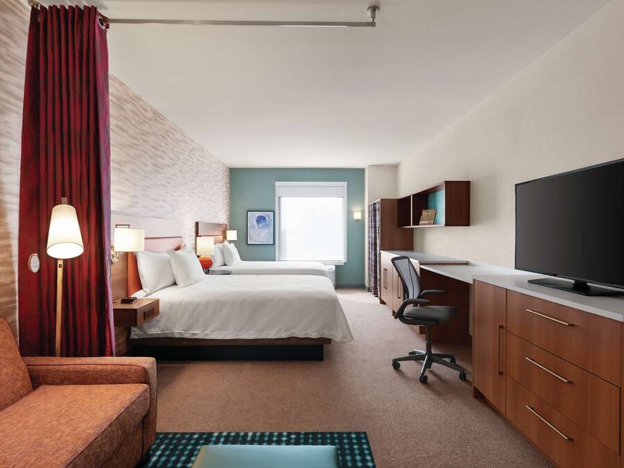 A hotel room with two beds, a desk with a TV, a chair, and a sofa.