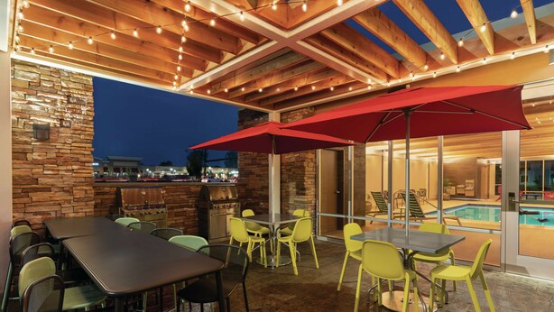 Un patio al aire libre con mesas y sillas, una parrilla y vistas a la piscina.