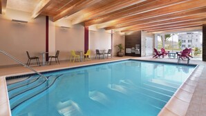 Una piscina con techo de madera, sillas y mesas alrededor del borde.