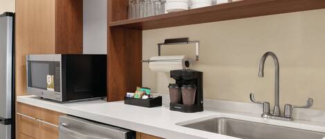 A kitchen with a stainless steel sink, a coffee maker, a microwave, and a dish rack.