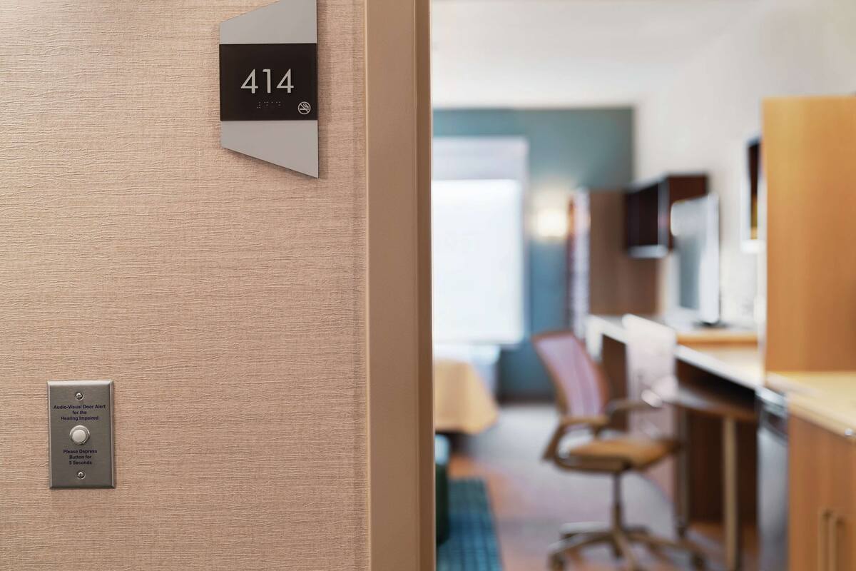 A hotel room with a door labeled '414', an audio-visual door alert system, and a view into the room featuring a desk, chairs, and a television.