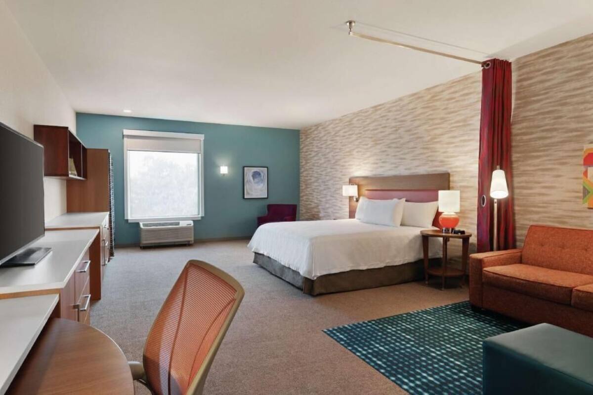 A hotel room with a bed, a desk, a chair, a TV, a lamp, and a couch.