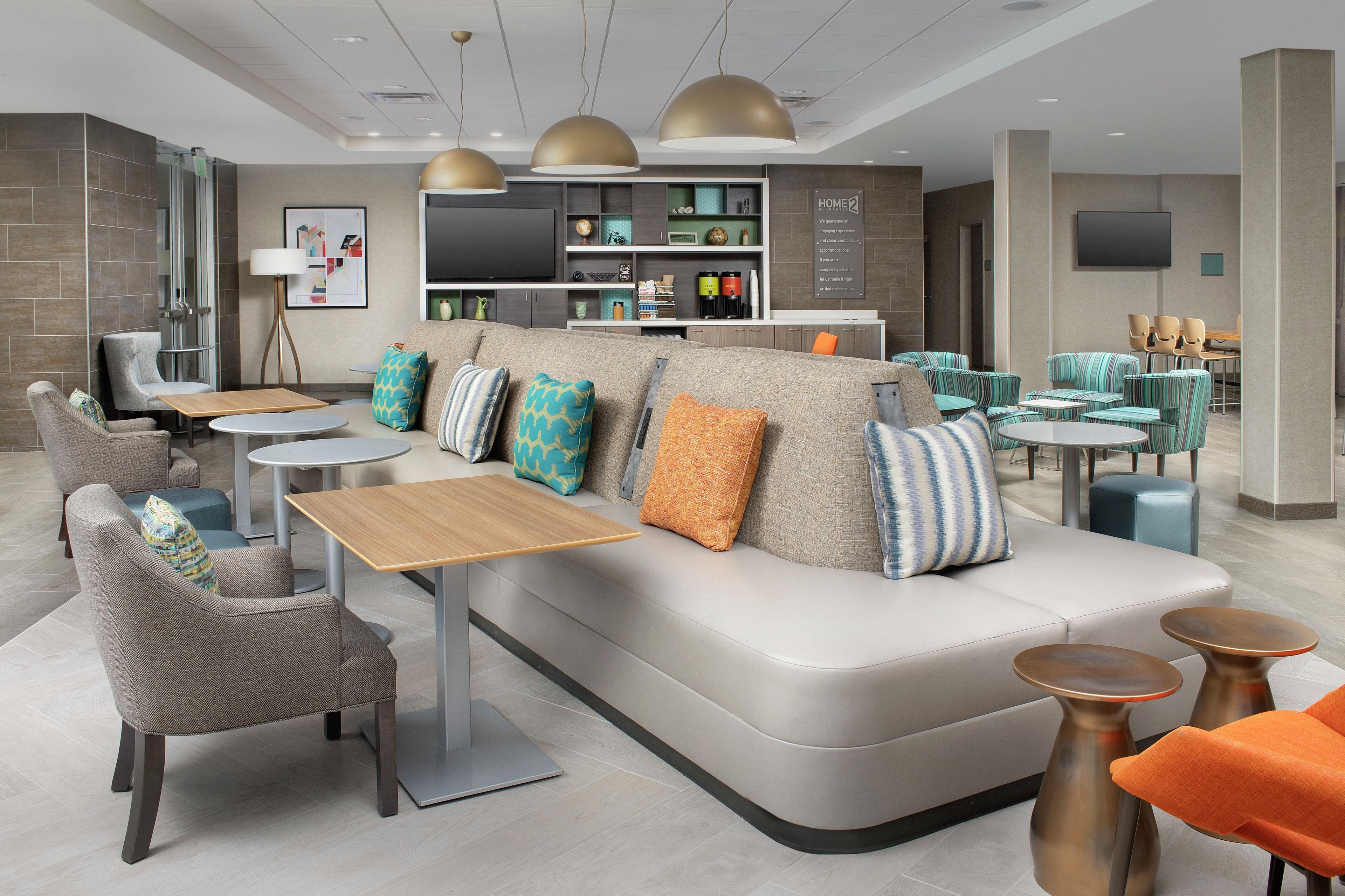 A modern hotel lobby with a sofa, chairs, tables, and a TV screen.