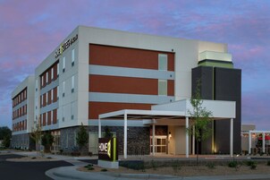 Un hotel moderno con un llamativo letrero de 'HOME 2 SUITES BY HILTON', una entrada cubierta y un frente de piedra.